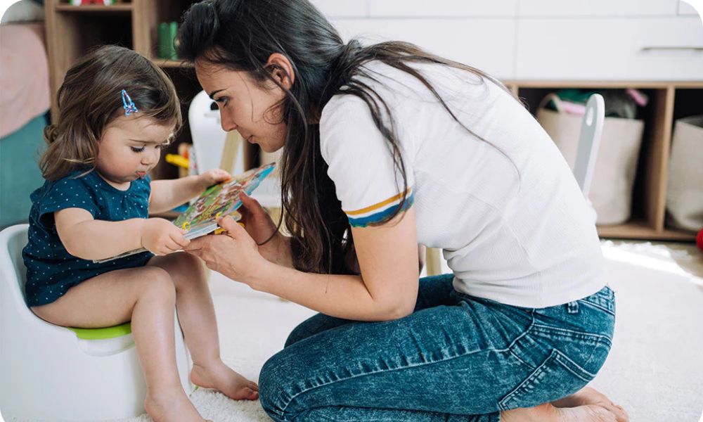A parent gently reading to a toddler sitting on a potty, creating a calm and encouraging potty training step by step routine at home.