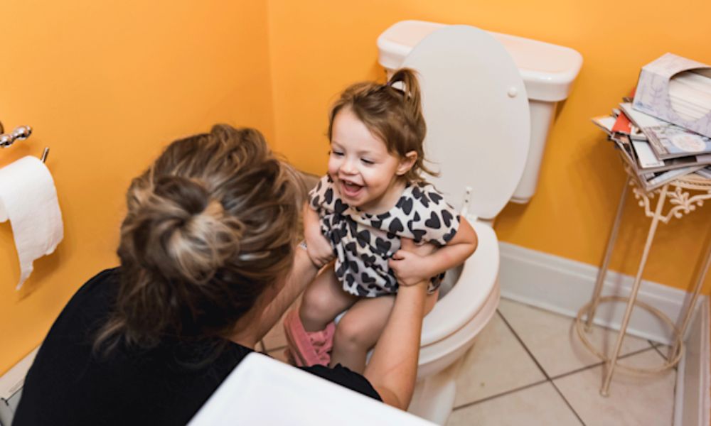 A smiling parent helps a happy toddler sit on the toilet during potty training step by step, showing encouragement and positive reinforcement.